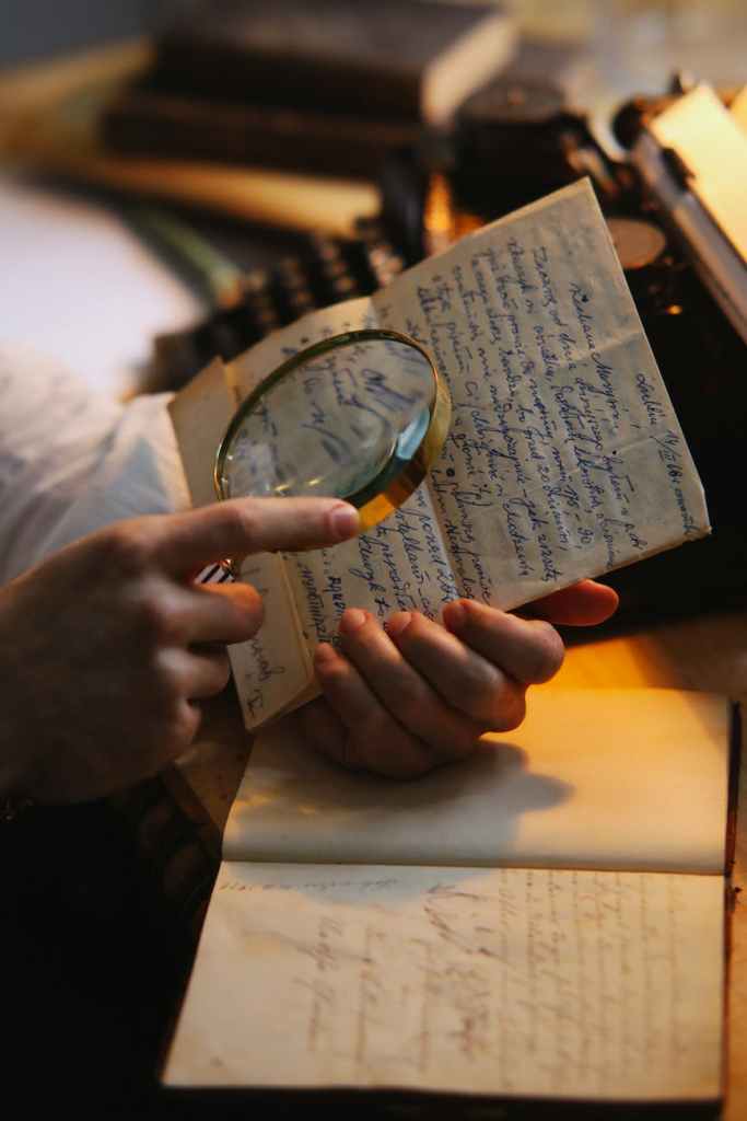 Photograph of a hand holding a magnifying glass to look at a hand-writtten letter.