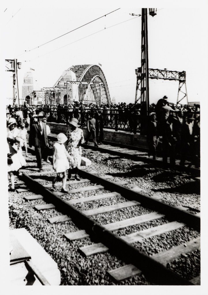 Photograph of a family walking amongst people walking along Sydney Harbour Bridge train tracks during opening celebrations in Sydney in 1932