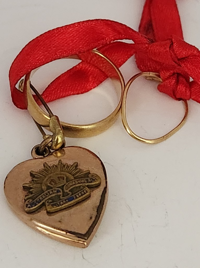 Sweetheart locket from World War Two tied with a red ribbon to a pin and two wedding rings. 