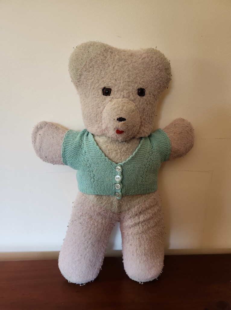 Photograph of a teddy bear approximately 50 years old wearing a button-up cardigan