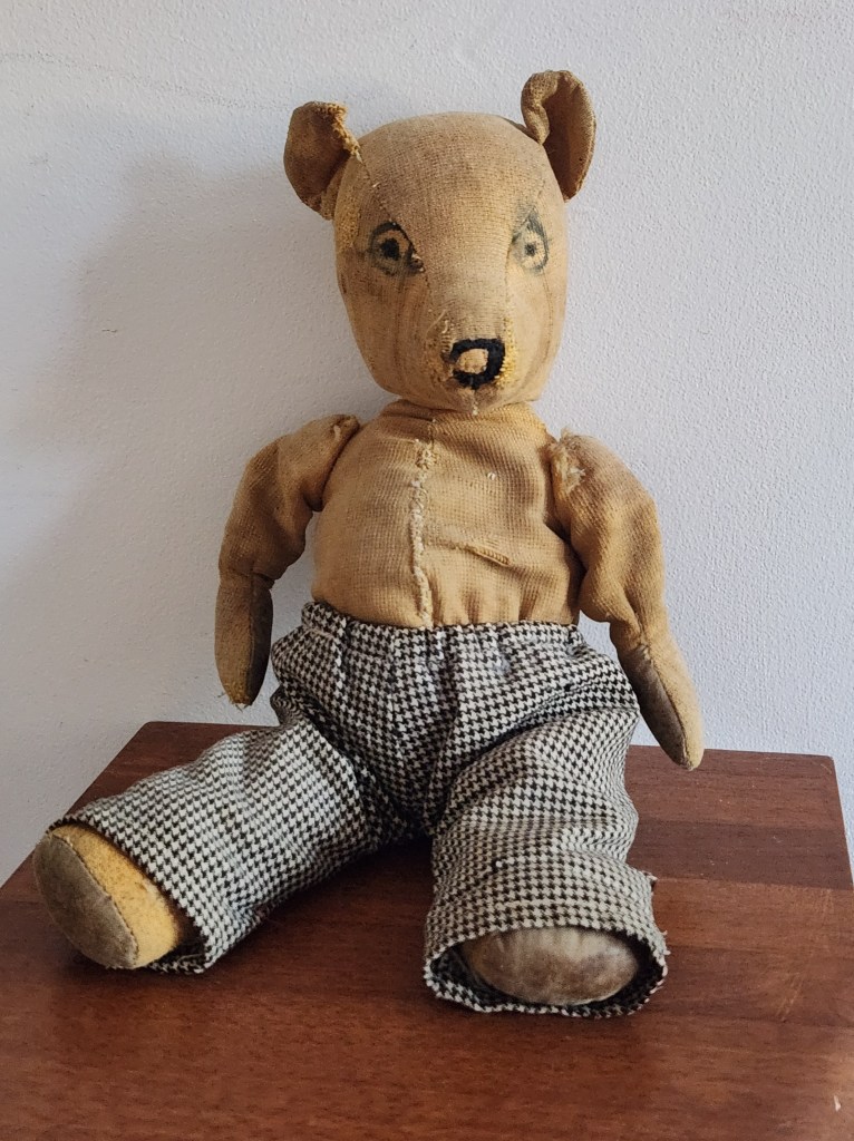 Photograph of a teddy bear approximately 75 years old wearing a pair of check pants